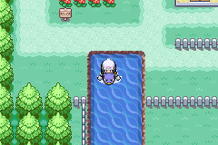 The player surfing on a Pokémon along a narrow channel of water beside a fenced route