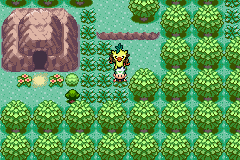 The player walking a wooded path towards a cave mouth in the rock face