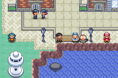 An overhead view of a town along the water, with several trainers and a round white object standing near the shore